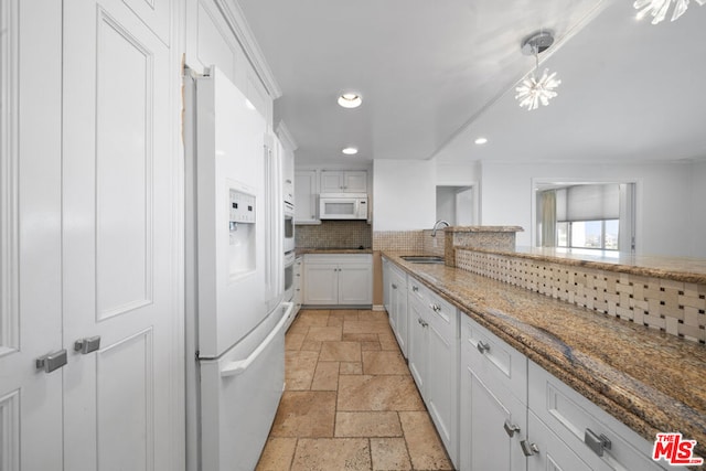 kitchen featuring white appliances, backsplash, sink, light stone countertops, and white cabinetry