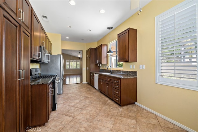 kitchen with appliances with stainless steel finishes, hanging light fixtures, dark stone counters, and a wealth of natural light