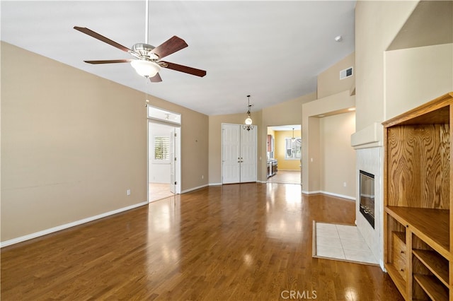 unfurnished living room with hardwood / wood-style floors, a tiled fireplace, ceiling fan, and high vaulted ceiling