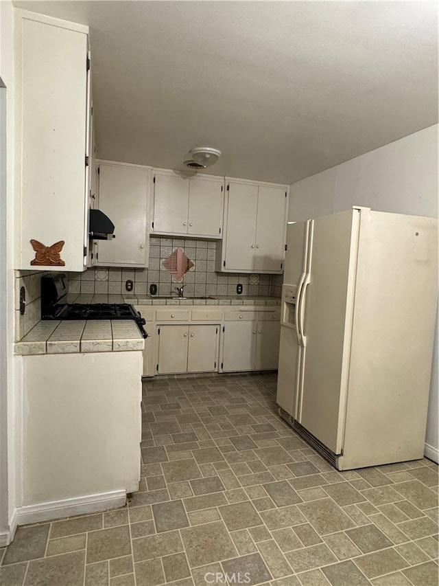 kitchen with black range oven, decorative backsplash, white cabinetry, white refrigerator with ice dispenser, and range hood