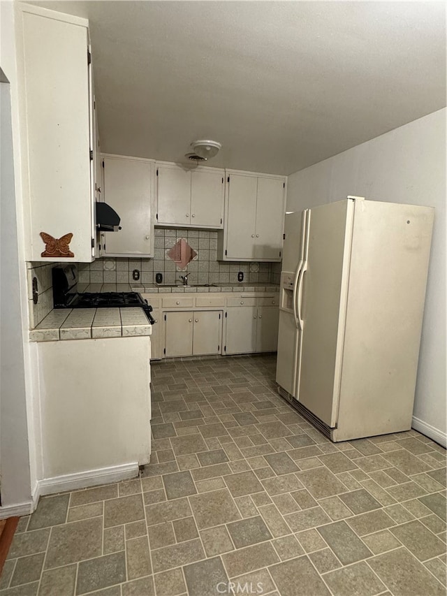 kitchen with white cabinets, tasteful backsplash, exhaust hood, white fridge with ice dispenser, and black stove