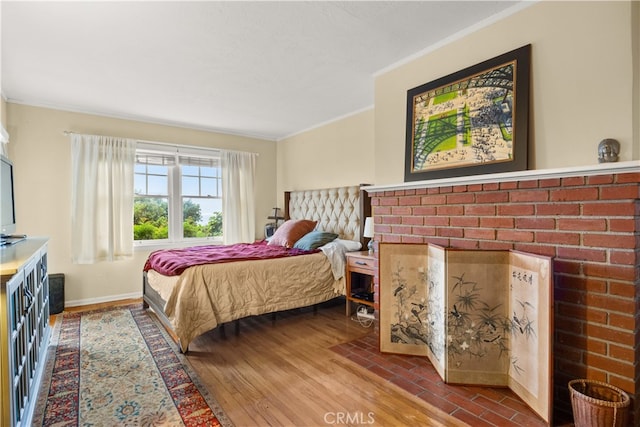 bedroom featuring ornamental molding, wood-type flooring, and a brick fireplace