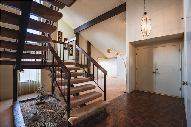 entryway with a chandelier, high vaulted ceiling, and dark tile patterned floors