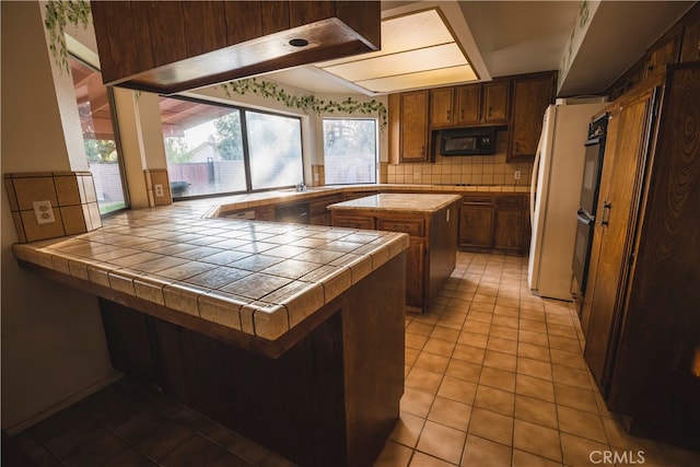 kitchen with tile counters, decorative backsplash, black appliances, and kitchen peninsula