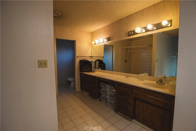 bathroom with toilet, tile patterned flooring, vanity, a tile shower, and a textured ceiling