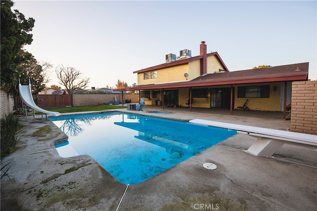 pool at dusk with a patio, a water slide, central AC, and a diving board