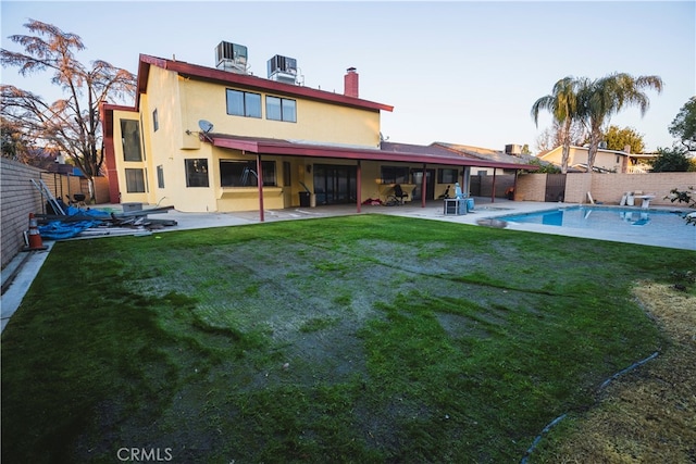 back of property featuring a lawn, central AC, a patio area, and a fenced in pool