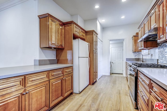 kitchen with white refrigerator, sink, backsplash, light wood-type flooring, and gas stove