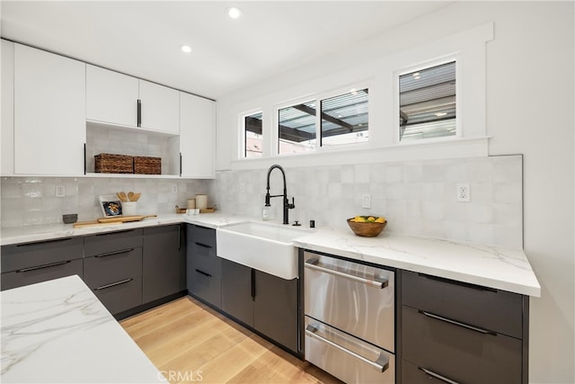 kitchen with decorative backsplash, light stone counters, sink, light hardwood / wood-style flooring, and white cabinetry