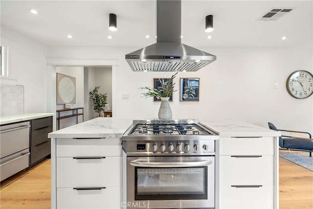 kitchen featuring white cabinetry, stainless steel range, light stone counters, and wall chimney range hood