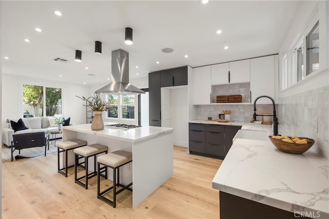 kitchen featuring island range hood, sink, light hardwood / wood-style flooring, a center island, and stainless steel gas stovetop