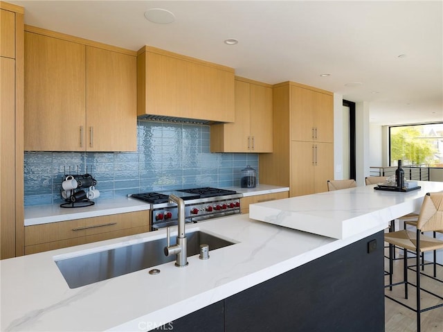 kitchen with high end range, decorative backsplash, light stone countertops, light wood-type flooring, and a kitchen bar