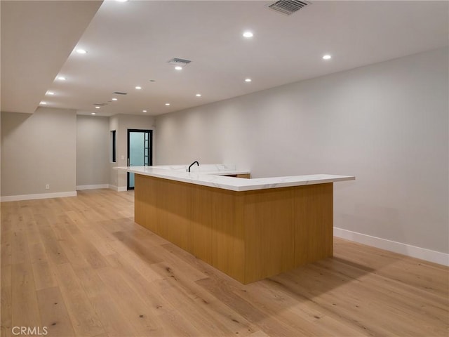 kitchen with a large island with sink, sink, and light wood-type flooring