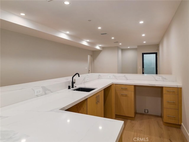 kitchen featuring kitchen peninsula, light wood-type flooring, light stone countertops, and sink