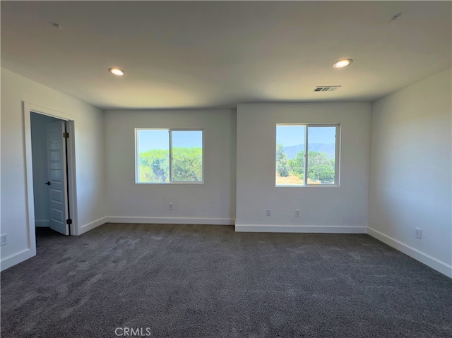 unfurnished room with dark colored carpet and plenty of natural light