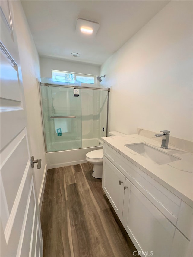 full bathroom with wood-type flooring, vanity, toilet, and bath / shower combo with glass door