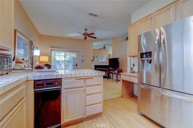 kitchen featuring stainless steel fridge with ice dispenser, ceiling fan, tile counters, light brown cabinets, and light wood-type flooring