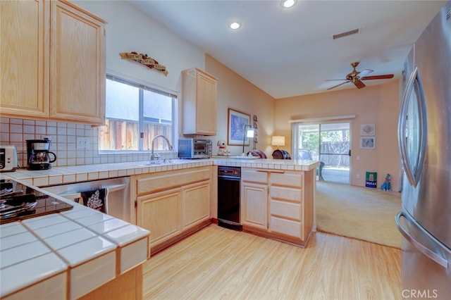 kitchen with backsplash, light hardwood / wood-style floors, kitchen peninsula, stainless steel refrigerator, and tile counters