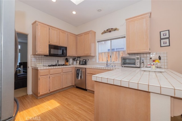 kitchen with tile countertops, decorative backsplash, kitchen peninsula, and black appliances