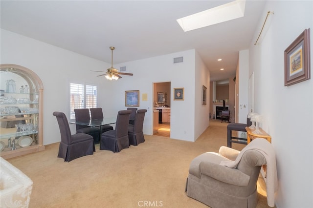 dining space with ceiling fan, light colored carpet, and a skylight