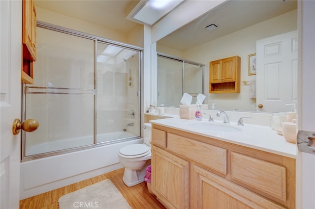 full bathroom with hardwood / wood-style flooring, combined bath / shower with glass door, vanity, and toilet