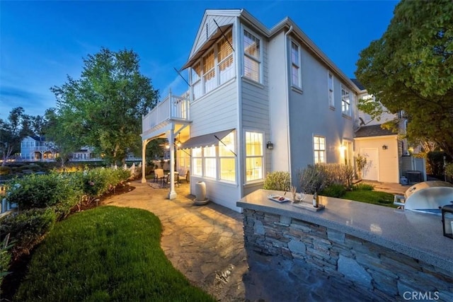 property exterior at dusk featuring an outdoor kitchen, a balcony, and a patio area