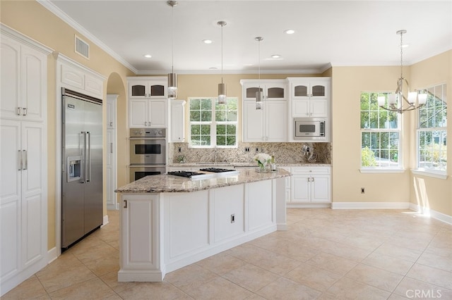 kitchen featuring decorative backsplash, built in appliances, decorative light fixtures, a kitchen island, and plenty of natural light