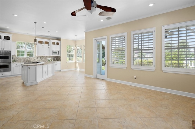 kitchen with backsplash, hanging light fixtures, white cabinets, and a healthy amount of sunlight