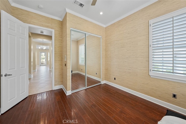 unfurnished bedroom with a closet, ornamental molding, ceiling fan with notable chandelier, and hardwood / wood-style flooring