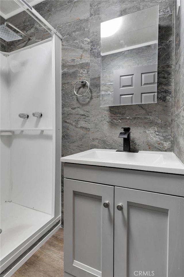 bathroom with vanity, wood finished floors, a stall shower, tile walls, and tasteful backsplash