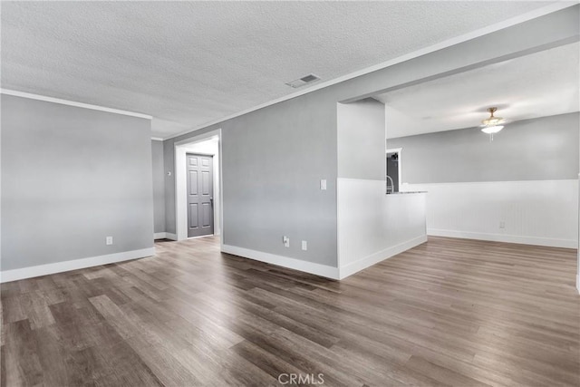 unfurnished room with wood finished floors, baseboards, visible vents, ornamental molding, and a textured ceiling