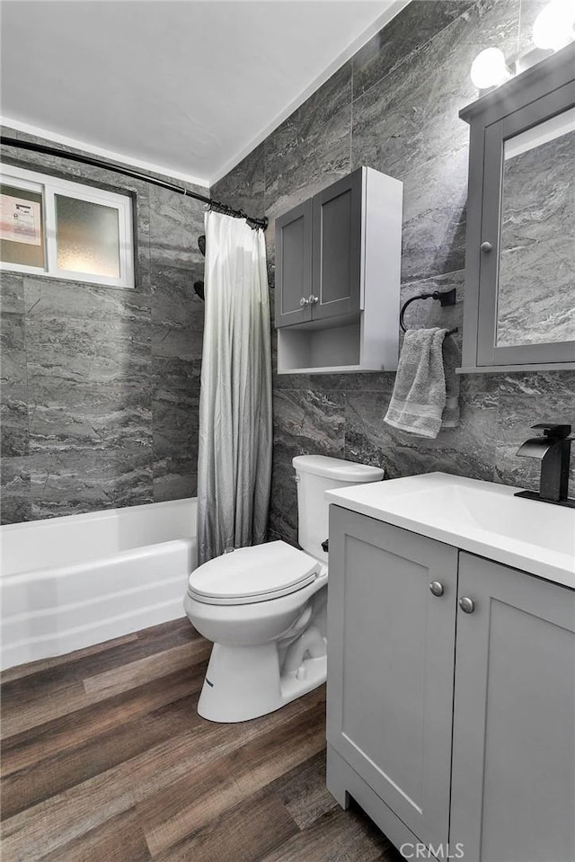 full bathroom with tile walls, toilet, wood finished floors, shower / bath combination with curtain, and vanity