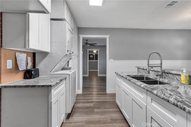 kitchen featuring a sink, light stone counters, wood finished floors, white cabinets, and stacked washer / drying machine