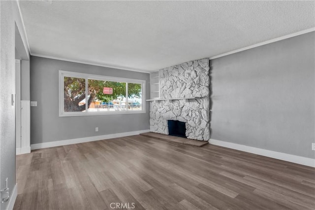 unfurnished living room featuring baseboards, a textured ceiling, a stone fireplace, and wood finished floors