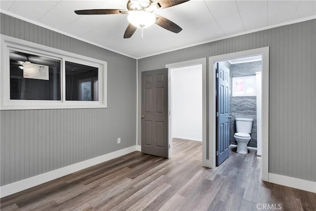 unfurnished bedroom featuring baseboards, ensuite bath, wood finished floors, and ornamental molding