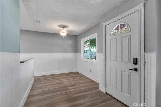 entrance foyer with wood finished floors, visible vents, a wainscoted wall, and a textured ceiling