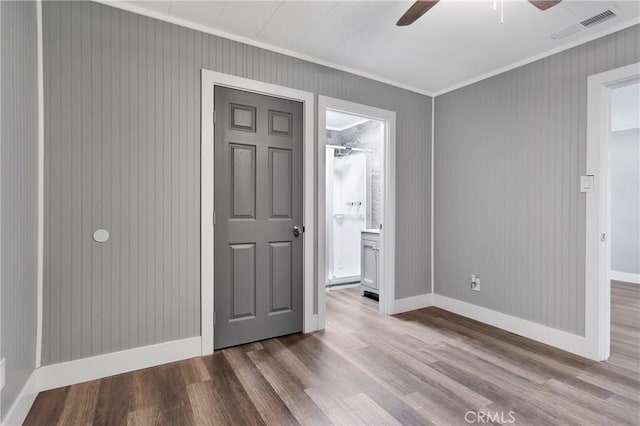 unfurnished bedroom featuring wood finished floors, baseboards, visible vents, ensuite bath, and ornamental molding