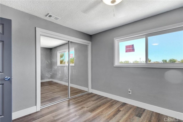 unfurnished bedroom featuring a textured ceiling, wood finished floors, visible vents, and baseboards