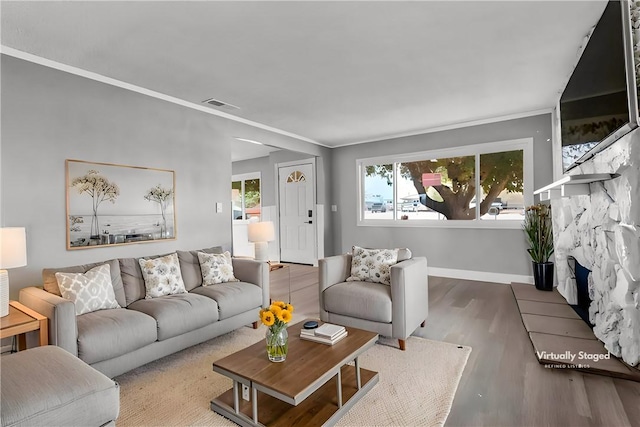 living room featuring visible vents, a stone fireplace, baseboards, and wood finished floors