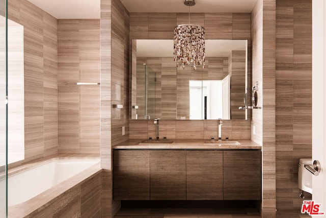 full bathroom with tile walls, independent shower and bath, an inviting chandelier, vanity, and toilet