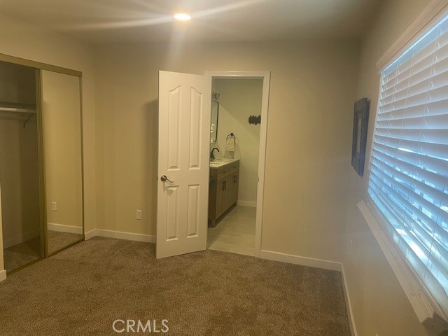 unfurnished bedroom featuring a closet, light carpet, multiple windows, and sink