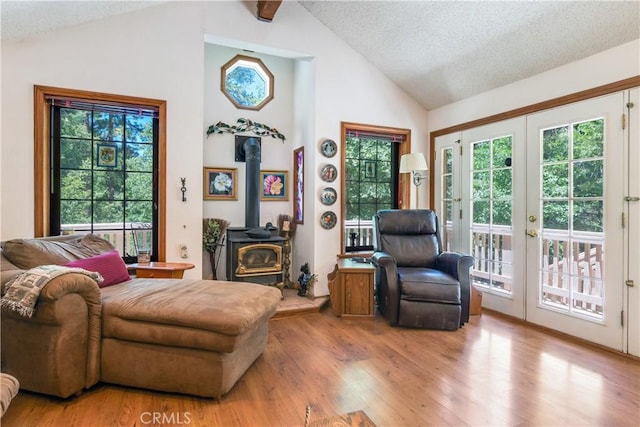 sitting room with high vaulted ceiling, a wood stove, light wood-type flooring, a textured ceiling, and french doors