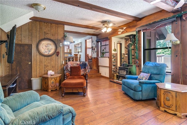 9339 Wood Rd, Forest Falls, CA 92339 - living room with a textured ceiling, wooden walls, a wood stove, light wood-style flooring, and a ceiling fan