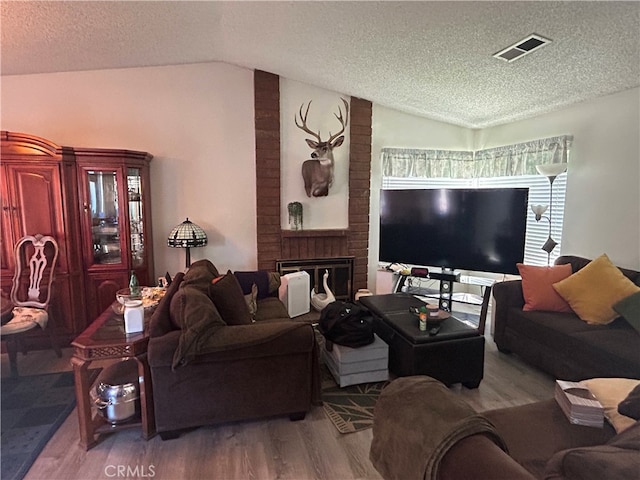 living room featuring lofted ceiling, a textured ceiling, hardwood / wood-style floors, and a fireplace