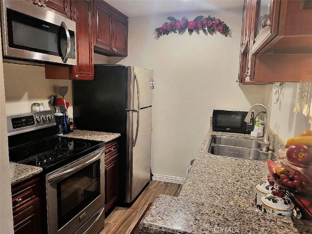 kitchen with light stone countertops, sink, light wood-type flooring, and stainless steel appliances