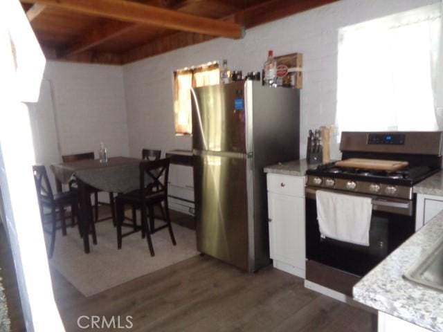 kitchen with beam ceiling, white cabinetry, light stone countertops, dark hardwood / wood-style floors, and appliances with stainless steel finishes