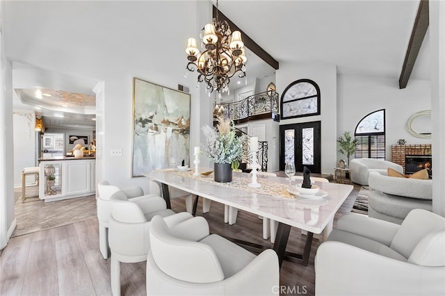 dining room with light hardwood / wood-style floors, beamed ceiling, a notable chandelier, a brick fireplace, and a towering ceiling