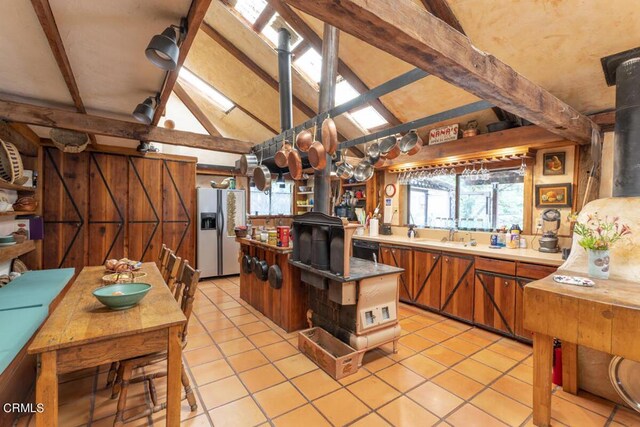 kitchen with vaulted ceiling with beams, light tile patterned floors, a wood stove, stainless steel refrigerator with ice dispenser, and dishwasher