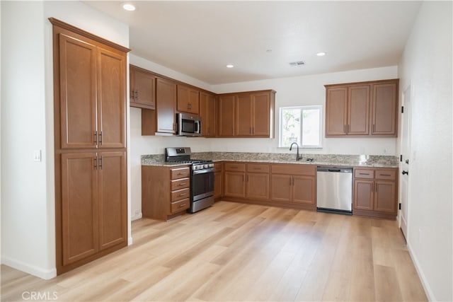 kitchen featuring stainless steel appliances, light stone countertops, light hardwood / wood-style floors, and sink