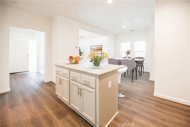 kitchen featuring baseboards, a breakfast bar, wood finished floors, a kitchen island, and light stone counters